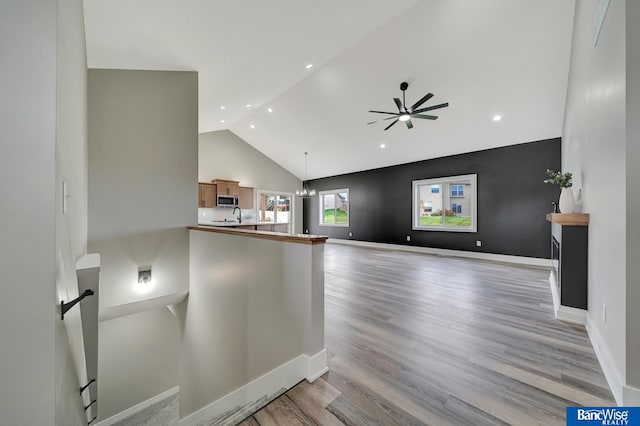 unfurnished living room featuring ceiling fan with notable chandelier, light hardwood / wood-style floors, and high vaulted ceiling