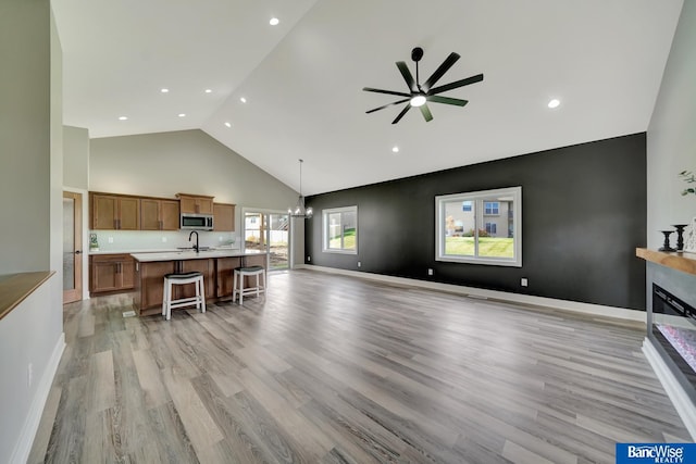 living room featuring ceiling fan with notable chandelier, light wood-type flooring, high vaulted ceiling, and sink