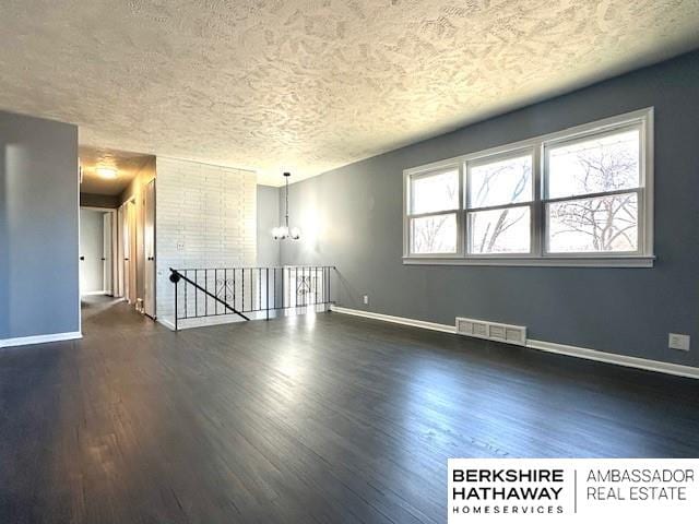 unfurnished room featuring a textured ceiling, dark hardwood / wood-style floors, and an inviting chandelier