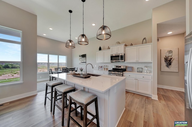 kitchen featuring stainless steel appliances, sink, white cabinets, hanging light fixtures, and an island with sink