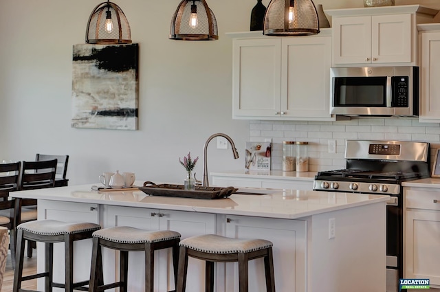 kitchen featuring stainless steel appliances, a kitchen bar, decorative backsplash, a center island with sink, and white cabinets