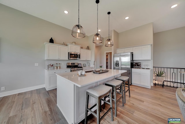 kitchen featuring hanging light fixtures, white cabinetry, stainless steel appliances, and a kitchen island with sink