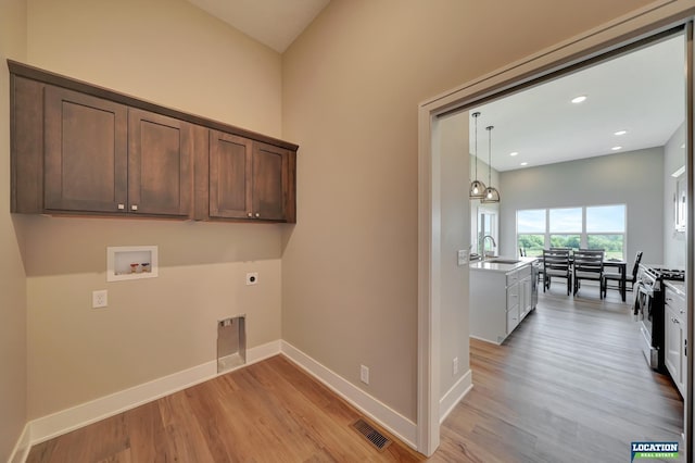 clothes washing area with electric dryer hookup, hookup for a washing machine, sink, and light hardwood / wood-style flooring