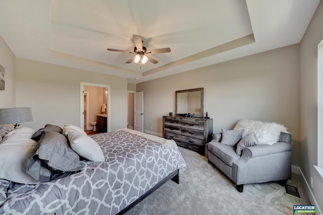 bedroom featuring a raised ceiling, ceiling fan, ensuite bathroom, and light colored carpet