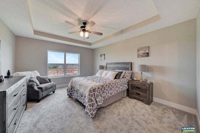 bedroom featuring a tray ceiling, ceiling fan, light carpet, and a textured ceiling