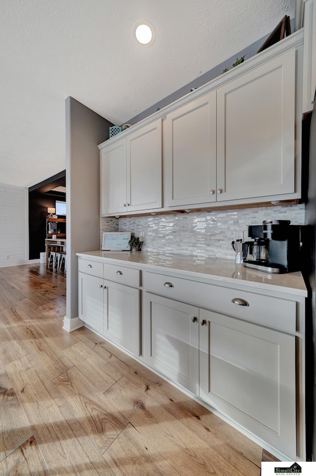 kitchen featuring decorative backsplash, light hardwood / wood-style flooring, white cabinets, and a textured ceiling