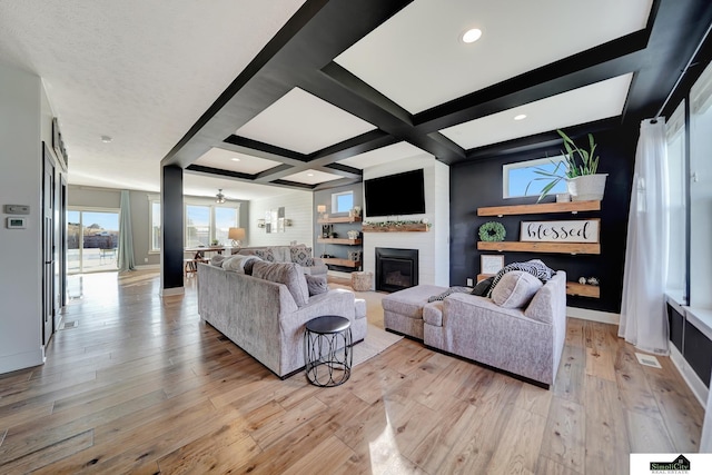 living room featuring beamed ceiling, light wood-type flooring, a large fireplace, and coffered ceiling