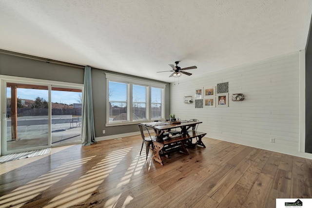 dining area featuring ceiling fan, wood-type flooring, a textured ceiling, and brick wall