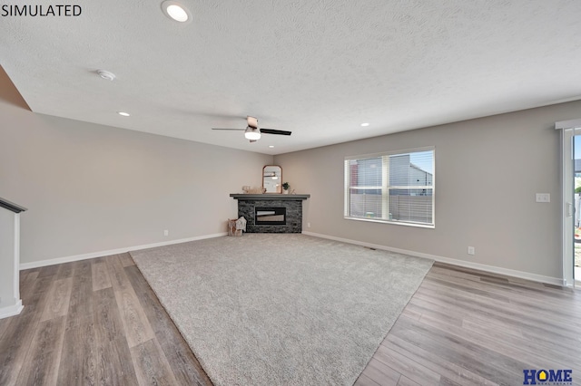 unfurnished living room featuring a fireplace, a textured ceiling, light hardwood / wood-style floors, and ceiling fan