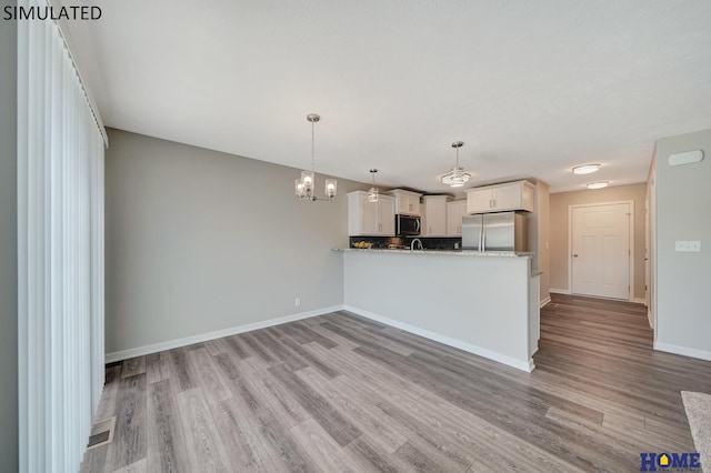 kitchen with kitchen peninsula, appliances with stainless steel finishes, light wood-type flooring, white cabinetry, and hanging light fixtures