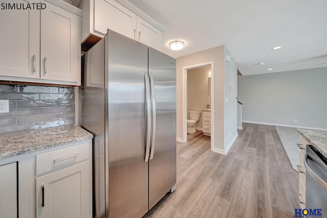 kitchen featuring stainless steel appliances, light stone counters, light hardwood / wood-style flooring, decorative backsplash, and white cabinets