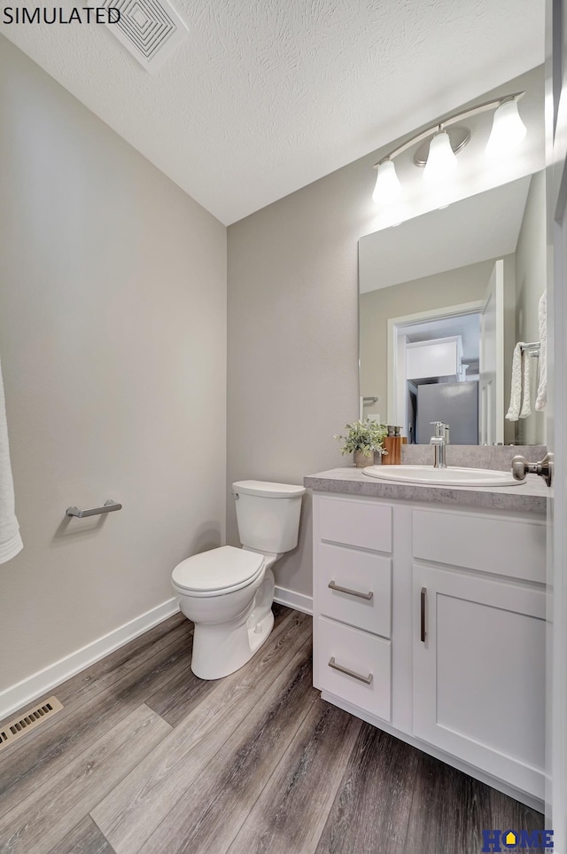 bathroom featuring vanity, toilet, wood-type flooring, and a textured ceiling