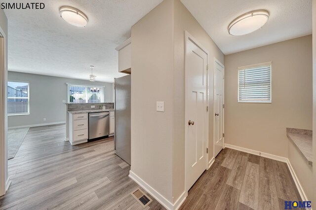 kitchen with a wealth of natural light, white cabinets, light wood-type flooring, and appliances with stainless steel finishes