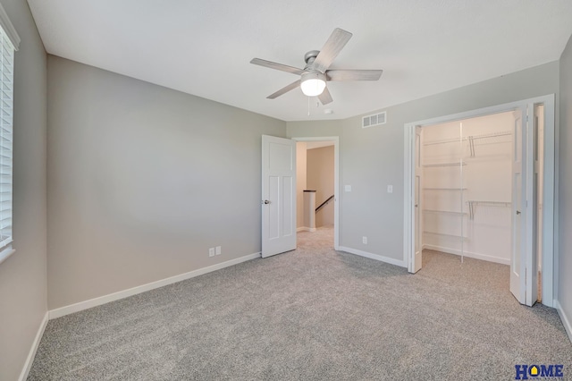 unfurnished bedroom with light carpet, a closet, a spacious closet, and ceiling fan