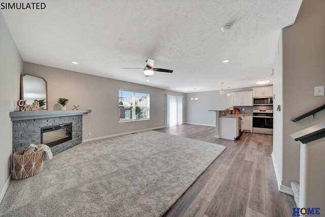 living room with ceiling fan, a fireplace, light hardwood / wood-style floors, and a textured ceiling