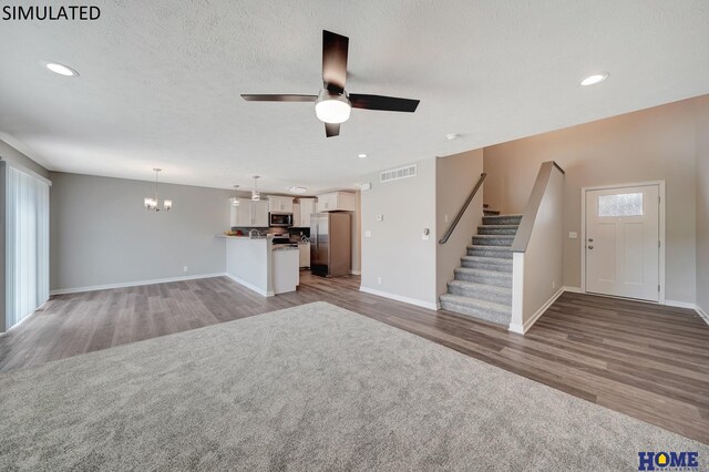 unfurnished living room with a textured ceiling, ceiling fan with notable chandelier, and light hardwood / wood-style flooring