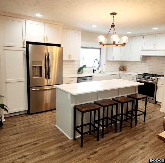 kitchen featuring a center island, hanging light fixtures, dark wood-type flooring, white cabinets, and appliances with stainless steel finishes