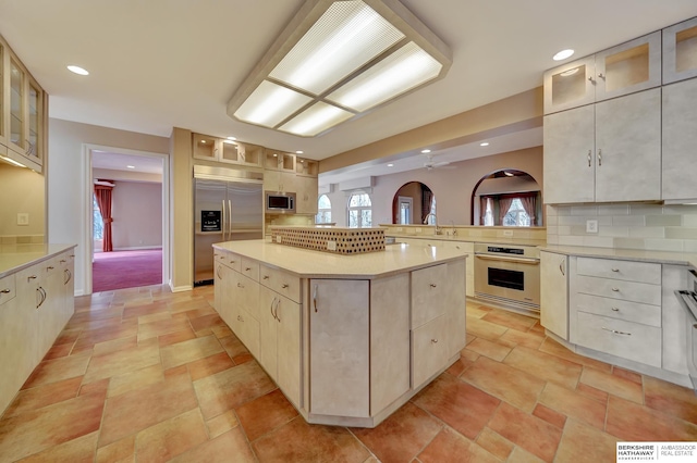 kitchen featuring tasteful backsplash, ceiling fan, sink, built in appliances, and a center island