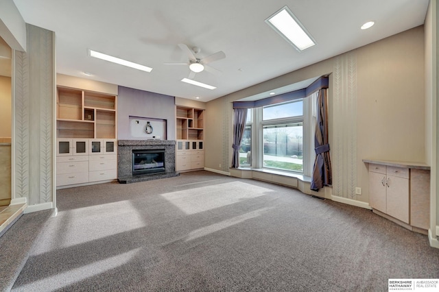 unfurnished living room with ceiling fan, carpet floors, built in shelves, and a premium fireplace