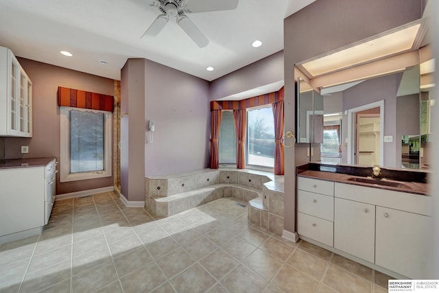 bathroom with tile patterned flooring, vanity, ceiling fan, and tiled bath