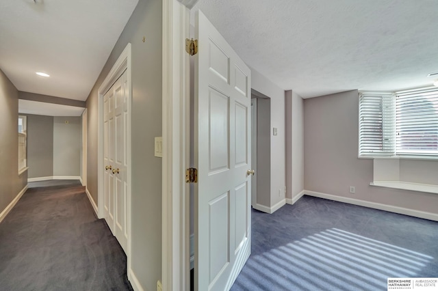 hallway featuring dark carpet and a textured ceiling