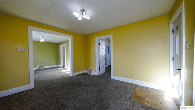 carpeted empty room with ceiling fan and a drop ceiling