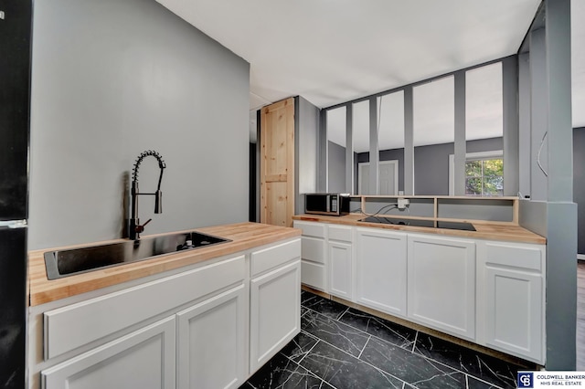 kitchen featuring butcher block counters, white cabinetry, and sink