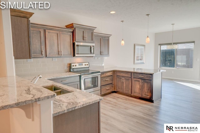 kitchen featuring sink, hanging light fixtures, light stone counters, kitchen peninsula, and appliances with stainless steel finishes