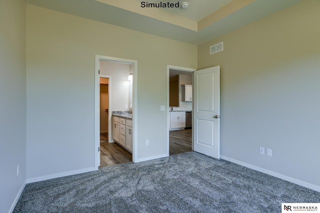 unfurnished bedroom with ensuite bathroom and dark carpet