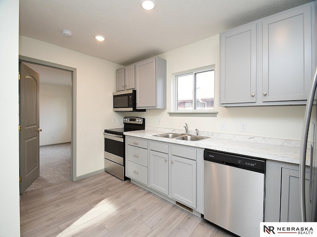 kitchen with appliances with stainless steel finishes, gray cabinetry, a textured ceiling, sink, and light hardwood / wood-style flooring