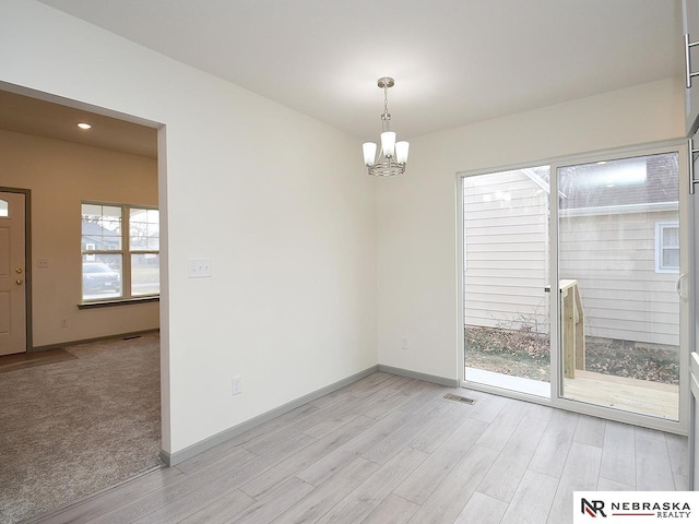 spare room featuring a chandelier and light hardwood / wood-style floors