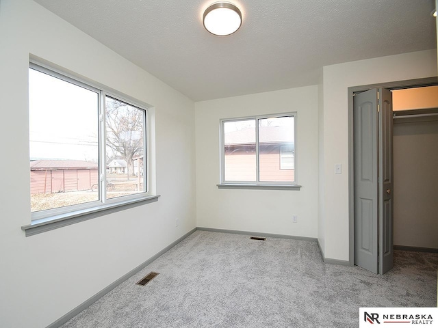 unfurnished bedroom with a textured ceiling, light carpet, and multiple windows