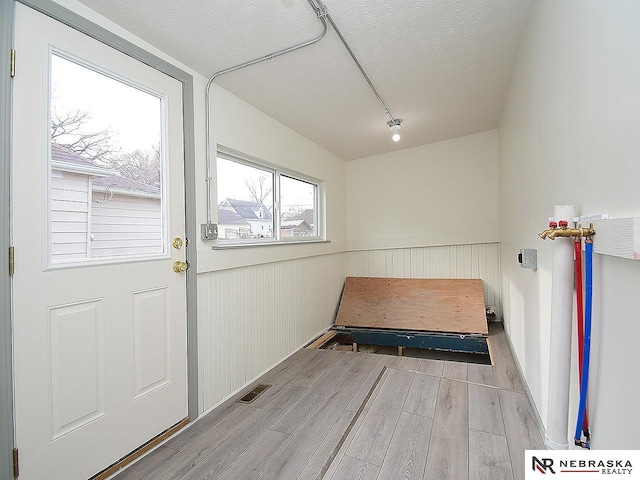 doorway featuring light hardwood / wood-style floors, a textured ceiling, and wooden walls