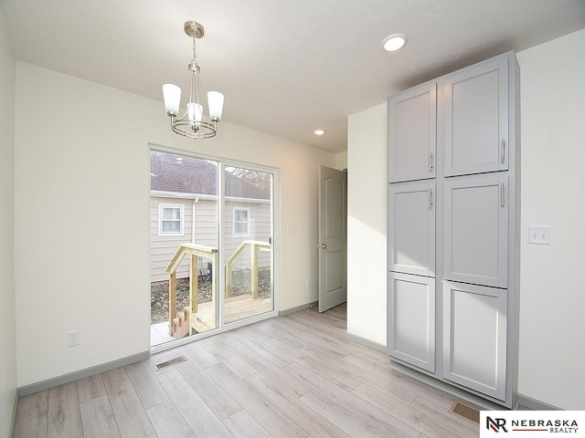 unfurnished dining area featuring a chandelier, a textured ceiling, and light hardwood / wood-style flooring