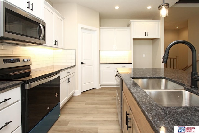 kitchen featuring white cabinets, appliances with stainless steel finishes, dark stone countertops, and sink