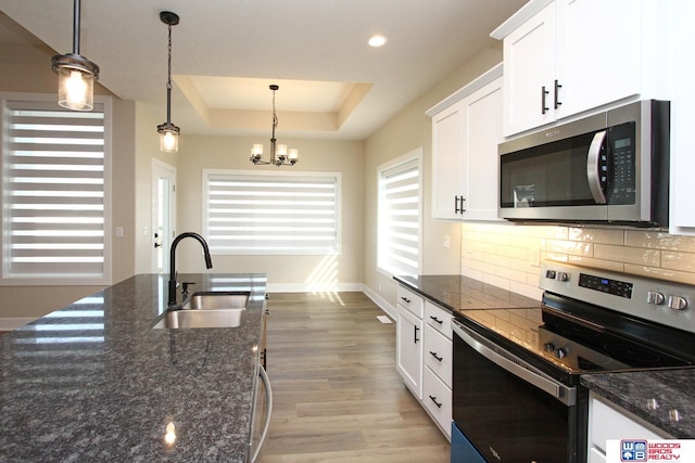 kitchen featuring white cabinetry, sink, dark stone counters, decorative light fixtures, and appliances with stainless steel finishes