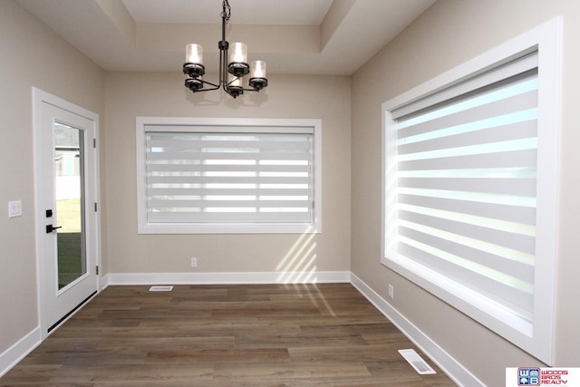 unfurnished dining area featuring a wealth of natural light, dark wood-type flooring, and an inviting chandelier