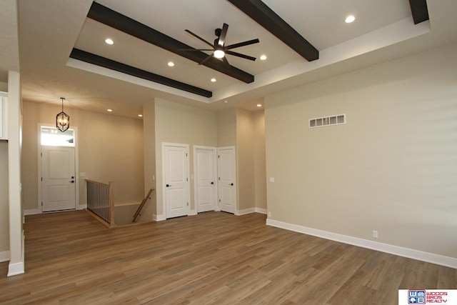 empty room with hardwood / wood-style floors, ceiling fan, a towering ceiling, a tray ceiling, and beam ceiling