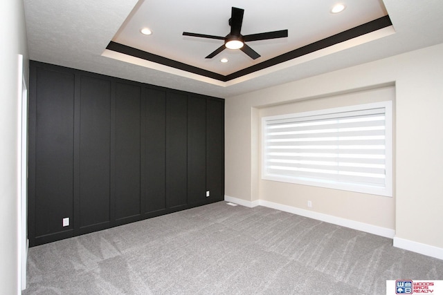 carpeted empty room with a raised ceiling and ceiling fan