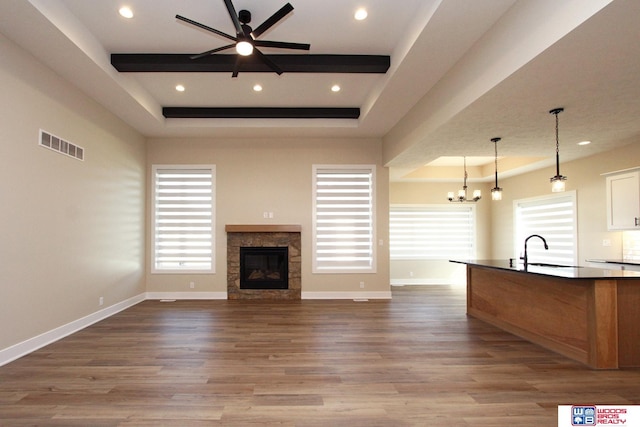 unfurnished living room featuring a tile fireplace, sink, a raised ceiling, light hardwood / wood-style flooring, and ceiling fan with notable chandelier