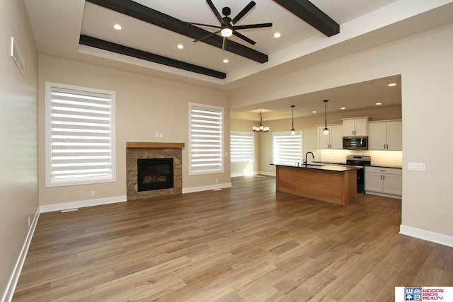 unfurnished living room featuring ceiling fan with notable chandelier, light wood-type flooring, a fireplace, and a wealth of natural light