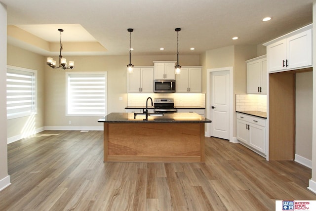 kitchen with light hardwood / wood-style flooring, stainless steel appliances, white cabinetry, and an island with sink