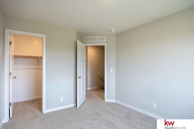 unfurnished bedroom featuring a walk in closet, light colored carpet, and a closet