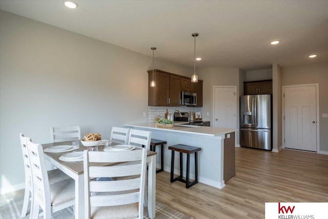 kitchen featuring dark brown cabinetry, tasteful backsplash, decorative light fixtures, light hardwood / wood-style flooring, and stainless steel appliances