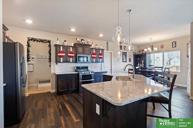 kitchen with stainless steel appliances, sink, pendant lighting, a center island with sink, and dark hardwood / wood-style floors