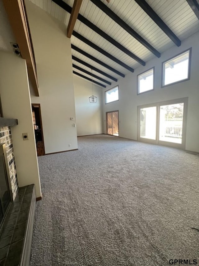 unfurnished living room with a tile fireplace, dark carpet, high vaulted ceiling, and beamed ceiling