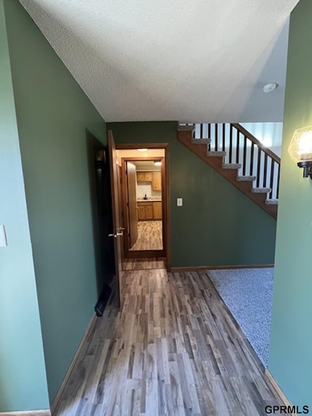 corridor with hardwood / wood-style flooring, lofted ceiling, and a textured ceiling