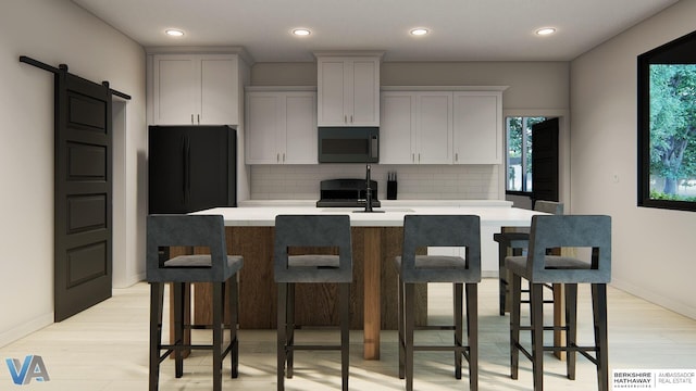 kitchen with a barn door, backsplash, an island with sink, light hardwood / wood-style floors, and black appliances