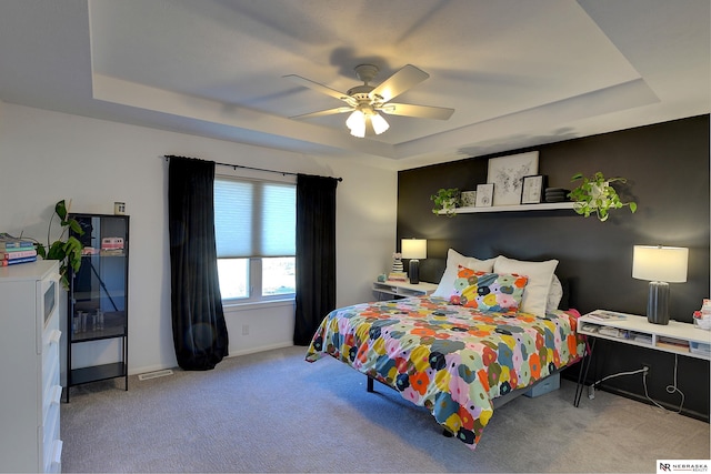 carpeted bedroom with a raised ceiling and ceiling fan