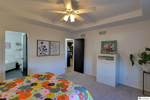 carpeted bedroom featuring a tray ceiling, connected bathroom, and ceiling fan